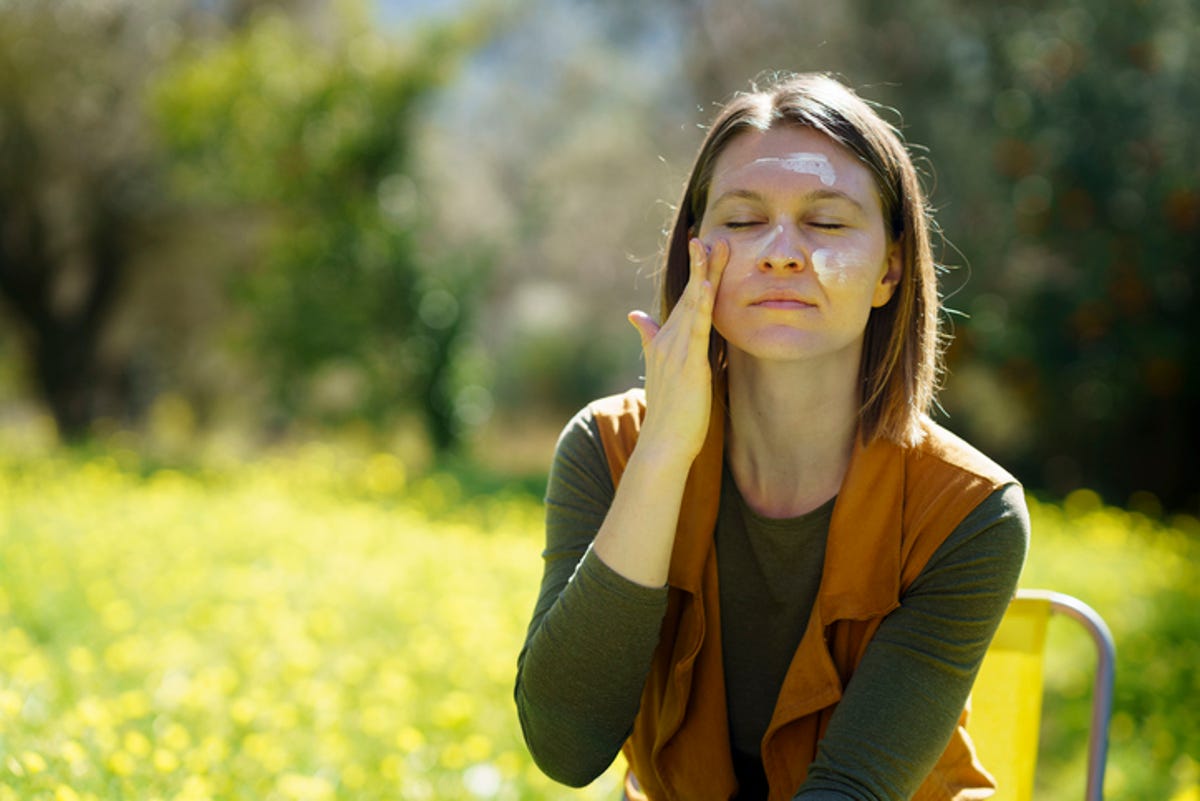 Woman applying sunscreen to her face while sitting outside.