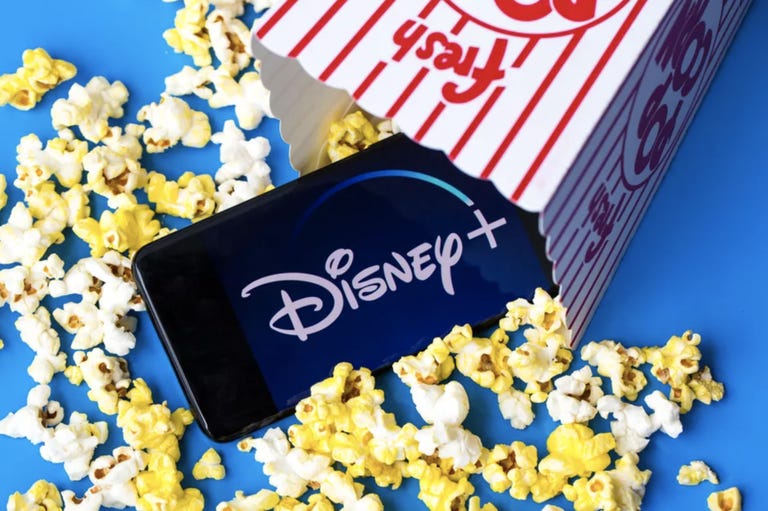 Disney Plus logo on a phone spilling out of a popcorn bag along with some popcorn