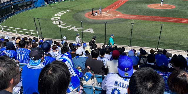 Fans wearing shirts with the name of baseball player Trevor Bauer and his number, watch his pitching at a stadium in Yokosuka, Japan, Sunday, April 16, 2023. Bauer pitched four innings Sunday for the Yokohama BayStars minor league team in Yokosuka as he prepares to pitch his first game for the Yokohama team.