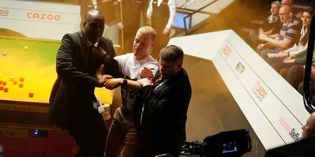 A Just Stop Oil protester is removed after jumping on the table and throwing orange powder during the match between Robert Milkins against Joe Perry during day three of the Cazoo World Snooker Championship at the Crucible Theatre, Sheffield. Picture date: Monday April 17, 2023.