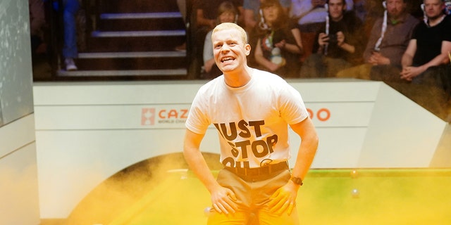 A Just Stop Oil protester jumps on the table and throws orange powder during the match between Robert Milkins against Joe Perry during day three of the Cazoo World Snooker Championship at the Crucible Theatre, Sheffield. Picture date: Monday April 17, 2023.