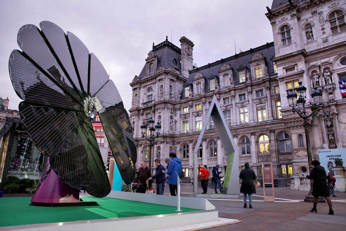 A Smartflower is open in front of an old hotel.