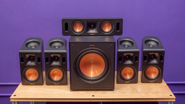 Klipsch Reference Cinema System 5.1.4 With Dolby Atmos surround sound speakers on a wood table with a purple background.