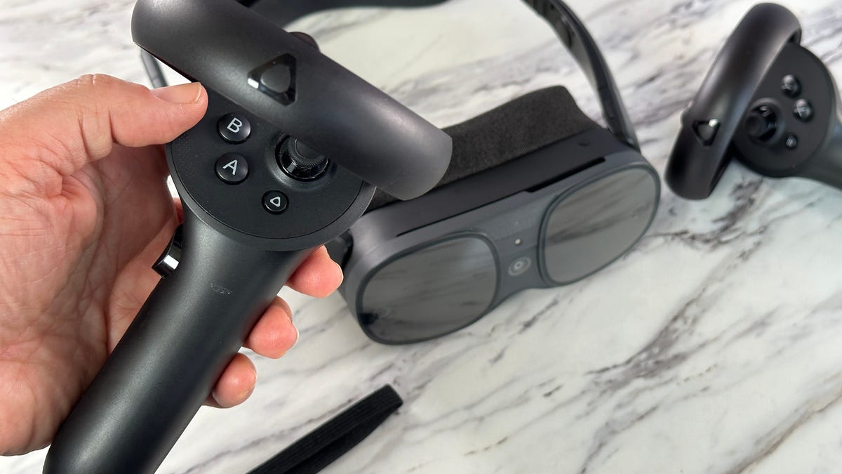 Holding a black VR game controller in front of a VR headset on a white table