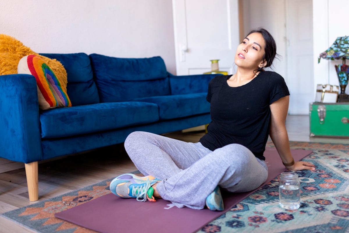 Woman experiencing fatigue while sitting on a yoga mat in her living room.