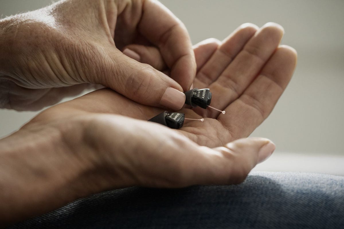 A tiny pair of hearing aids in a person's palm