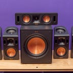 Klipsch Reference Cinema System 5.1.4 With Dolby Atmos surround sound speakers on a wood table with a purple background.