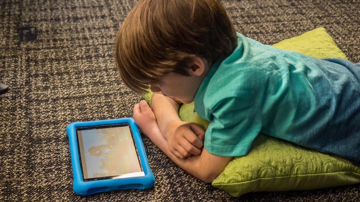 A kid laying on the floor and using a tablet.