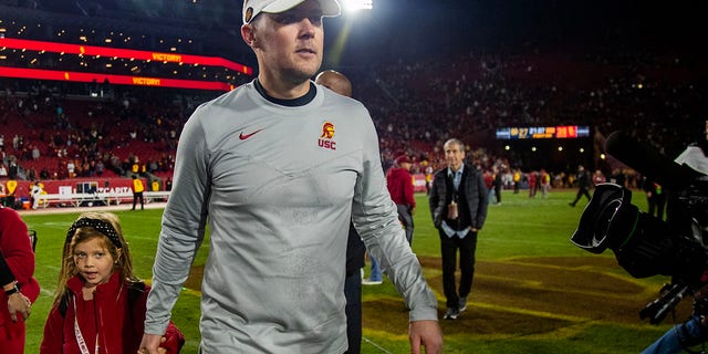 USC head coach Lincoln Riley holds his daughters hand as he leaves the field after the Trojans beat Notre Dame at the Coliseum on Nov. 26, 2022, in Los Angeles.