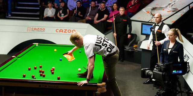 A Just Stop Oil protester jumps on the table and throws orange powder during the match between Robert Milkins against Joe Perry during day three of the Cazoo World Snooker Championship at the Crucible Theatre, Sheffield. Picture date: Monday April 17, 2023.