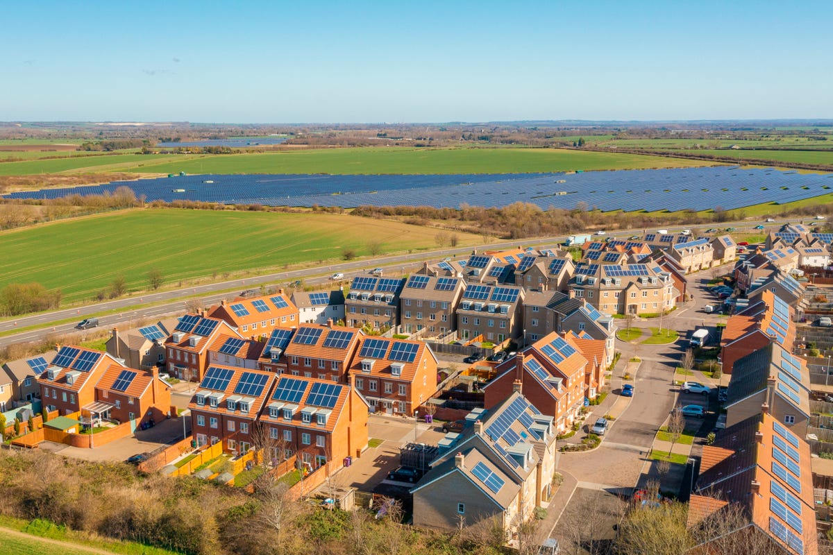 Homes with roof top solar panels in front of a large solar farm.